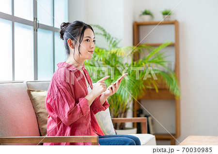 ソファでくつろぎながらスマホを操作する女性。 ソファでくつろぎながらスマホを操作する女性。 70030985
