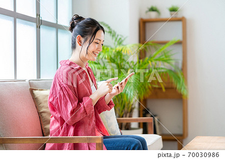 ソファでくつろぎながらスマホを操作する女性。 70030986