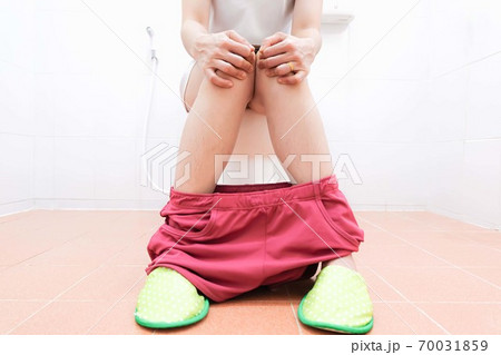 Women wearing white sleepwear, Sitting on the toilet Hand holding the stomach,standing in the toilet, Holding a toilet paper, bent, stomachache health care concept Women wearing white sleepwear, Sitting on the toilet Hand holding the stomach,standing in the toilet, Holding a toilet paper, bent, stomachache health care concept 70031859