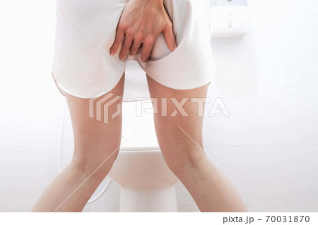 Women wearing white sleepwear, Sitting on the toilet Hand holding the stomach,standing in the toilet, Holding a toilet paper, bent, stomachache health care concept 70031870