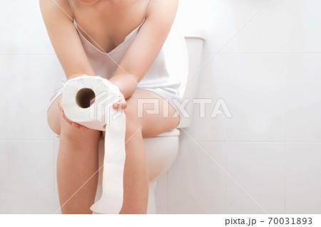 Women wearing white sleepwear, Sitting on the toilet Hand holding the stomach,standing in the toilet, Holding a toilet paper, bent, stomachache health care concept 70031893