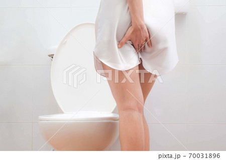 Women wearing white sleepwear, Sitting on the toilet Hand holding the stomach,standing in the toilet, Holding a toilet paper, bent, stomachache health care concept Women wearing white sleepwear, Sitting on the toilet Hand holding the stomach,standing in the toilet, Holding a toilet paper, bent, stomachache health care concept 70031896