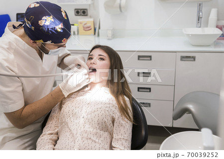 Young bearded male dentist drilling tooth to 70039252