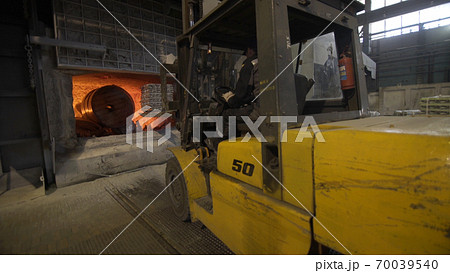 Camera is moving forward of Loader loads aluminum ingots into a blast furnace. Aluminium foundry furnace loaded with metal. Red hot flames glowing and liquid melting. 70039540