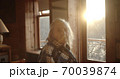 portrait of a beautiful old Granny in a cozy wooden room against the background of sunset or sunrise. 70039874