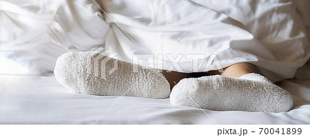 Woman feet in warm woolen socks on white bedclothes. Close up of young woman lying in bed at home. 70041899