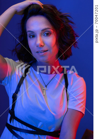 Woman corrects her hair looking at camera on blue background while posing in neon studio lighting. High quality photo 70047201