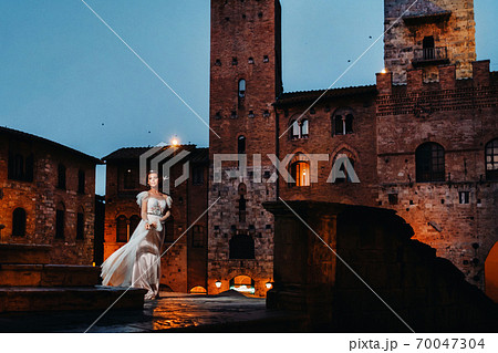 A bride in a white dress in the old town of San Gimignano.A girl walks around the city in Italy.Tuscany. 70047304