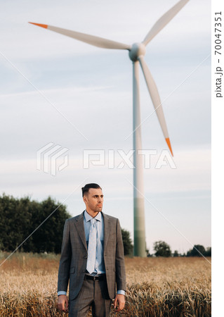 Portrait of a businessman in a gray suit on a wheat field against the background of a windmill and the evening sky 70047351