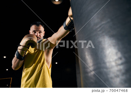 Athletic person in yellow shirt punching a bag Athletic person in yellow shirt punching a bag 70047468