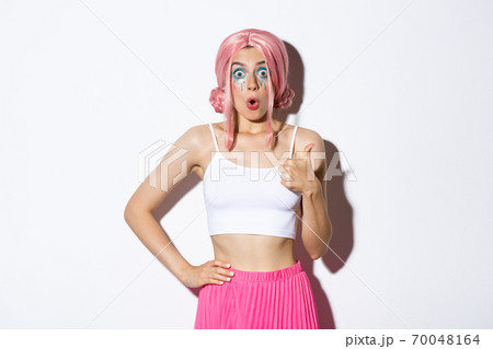 Portrait of impressed cute girl in party wig, looking amazed, showing thumbs-up in approval, like something good, standing over white background 70048164