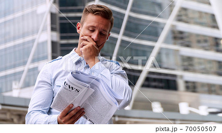 Businessman reading newspaper feeling serious while standing in urban background Businessman reading newspaper feeling serious while standing in urban background 70050507