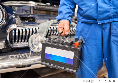 Engine engineer is replacing car battery because car battery is depleted. concept car maintenance. Against the background of a retro car of the 50s 70053810