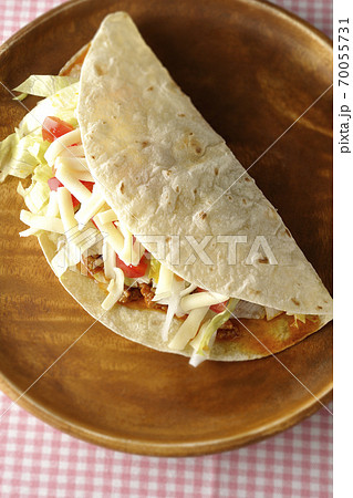丸い木製皿の上に置かれたチーズやミニトマトや挽き肉などが入ったタコス(俯瞰) 丸い木製皿の上に置かれたチーズやミニトマトや挽き肉などが入ったタコス(俯瞰) 70055731