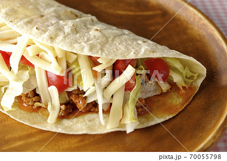 丸い木製皿の上に置かれたチーズやミニトマトや挽き肉などが入ったタコス 丸い木製皿の上に置かれたチーズやミニトマトや挽き肉などが入ったタコス 70055798