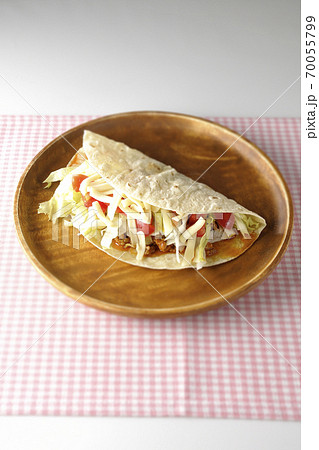 丸い木製皿の上に置かれたチーズやミニトマトや挽き肉などが入ったタコス 丸い木製皿の上に置かれたチーズやミニトマトや挽き肉などが入ったタコス 70055799