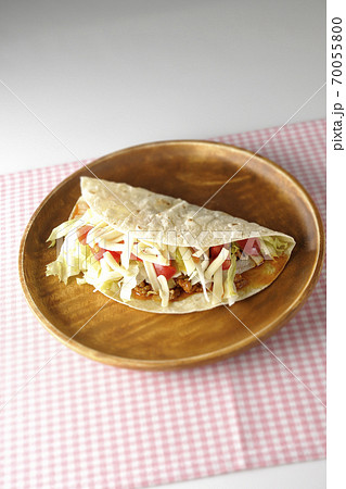 丸い木製皿の上に置かれたチーズやミニトマトや挽き肉などが入ったタコス 丸い木製皿の上に置かれたチーズやミニトマトや挽き肉などが入ったタコス 70055800