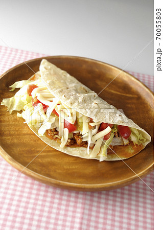 丸い木製皿の上に置かれたチーズやミニトマトや挽き肉などが入ったタコス 丸い木製皿の上に置かれたチーズやミニトマトや挽き肉などが入ったタコス 70055803