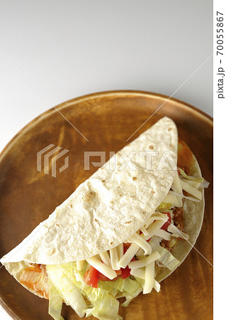丸い木製皿の上に置かれたチーズやミニトマトや挽き肉などが入ったタコス（白背景、俯瞰） 70055867