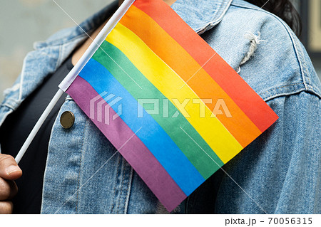 Asian lady wearing blue jean jacket or denim shirt and holding rainbow color flag, symbol of LGBT pride month celebrate annual in June social of gay, lesbian, bisexual, transgender, human rights. 70056315