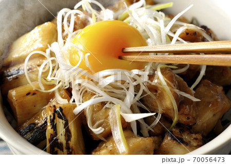 炭火で焼いた焼き鳥の上に白髪葱と卵黄を乗せた熱々ヤキトリ丼の黄身を箸で割って食べる 70056473