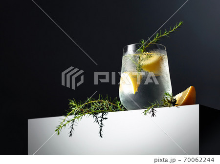 Alcohol drink (gin tonic cocktail) with lemon, juniper branch, and ice on a dark reflective background. 70062244
