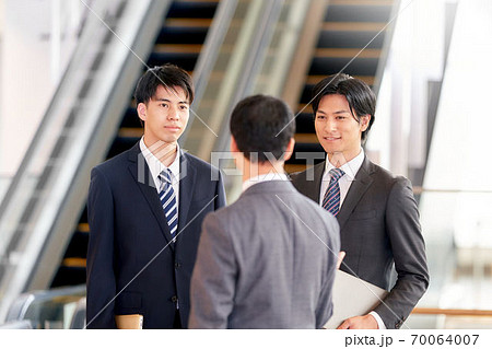 エスカレーター前で会話をするビジネスマン 70064007