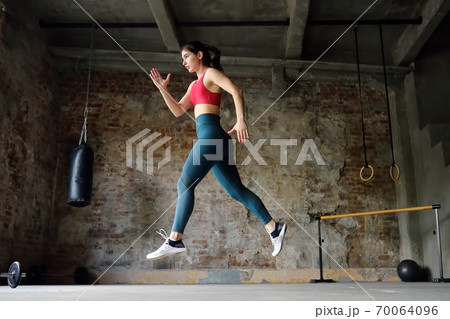 Sporty woman during HIIT workout. Sportswoman jumping high in the process of training in the gym Sporty woman during HIIT workout. Sportswoman jumping high in the process of training in the gym 70064096