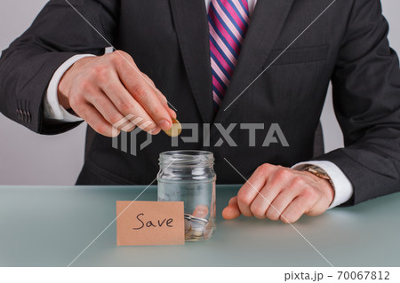 Male hand putting coins into glass jar for saving money. Male hand putting coins into glass jar for saving money. 70067812