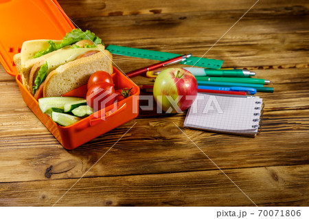 Back to school concept. School supplies, apple and lunch box with sandwiches and fresh vegetables on a wooden desk 70071806