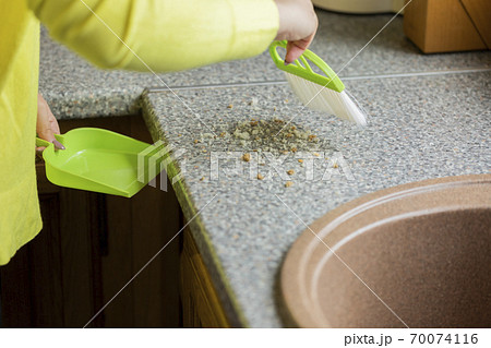 Close up person sweeps crumbs off table with brush and dustpan set for kitchen Close up person sweeps crumbs off table with brush and dustpan set for kitchen 70074116