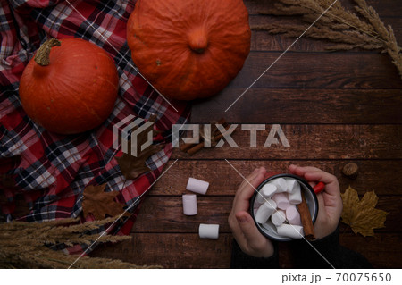 cup of cocoa with marshmallows in the palms of a child on a wooden table  70075650