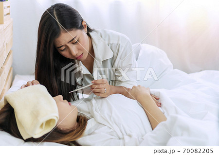 Sick woman have good friend to take care of her, having temperature check with thermometer.  70082205