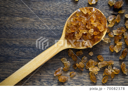 Natural organic brown crystal rock sugar in wooden spoon over wooden background. 70082378
