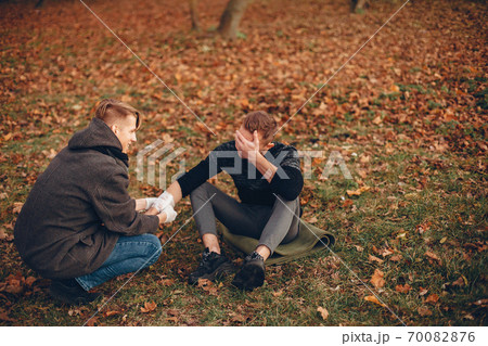 Guy bandages his friend's hand Guy bandages his friend's hand 70082876