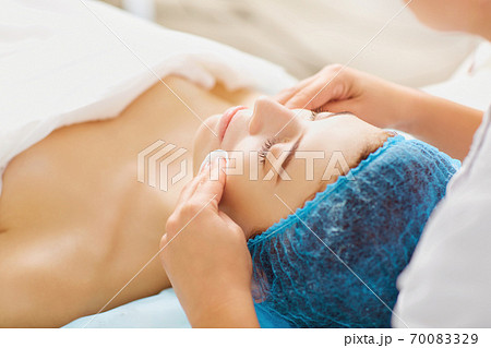 The hands of a cosmetologist clean the face of a woman. The hands of a cosmetologist clean the face of a woman. 70083329