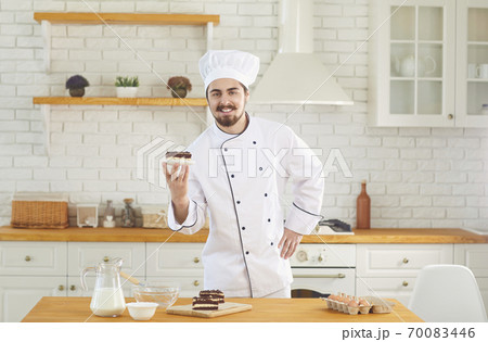 Confectioner man smiles while standing with cake in his hands at the kitchen bakery Confectioner man smiles while standing with cake in his hands at the kitchen bakery 70083446