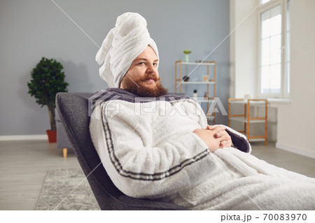 Funny strange fat bearded man in a bathrobe does spa treatments on his face rests in a room 70083970