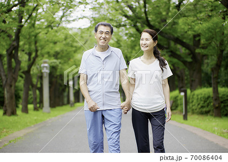 公園を手を繋いでウオーキングするシニアの夫婦 70086404