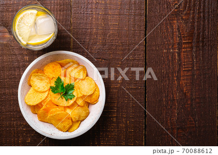 Fresh ice cold water drink with lemon near to fried potato chips with parsley leaf in wooden bowl on wood backdrop, top view copy space 70088612