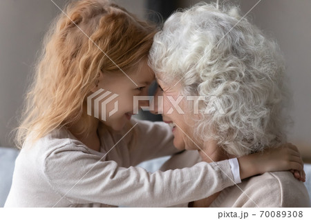 Close up smiling mature grandmother and little granddaughter touching foreheads Close up smiling mature grandmother and little granddaughter touching foreheads 70089308