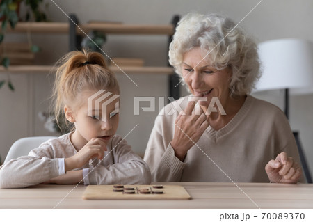 Happy mature grandmother and little granddaughter playing wooden board game 70089370