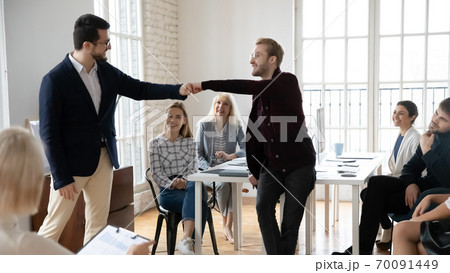 Smiling male colleagues give fist bump greeting Smiling male colleagues give fist bump greeting 70091449