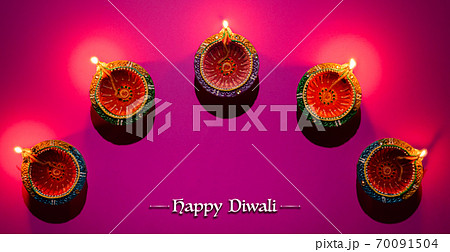 Happy Diwali - Clay Diya lamps lit during Dipavali, Hindu festival of lights celebration. Colorful traditional oil lamp diya on pink background 70091504