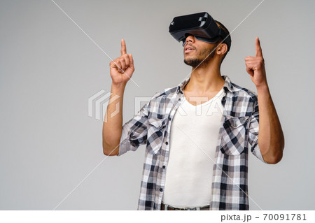 Young African-American young man wearing vr virtual reality headset over light grey background Young African-American young man wearing vr virtual reality headset over light grey background 70091781