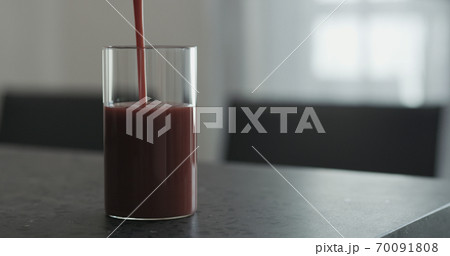 pour berry smoothie in highball glass on concrete countertop 70091808