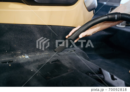 Worker hand with vacuum cleaner cleans car trim 70092818