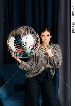 Beautiful young woman in grey sweater and disco ball at home 70093749