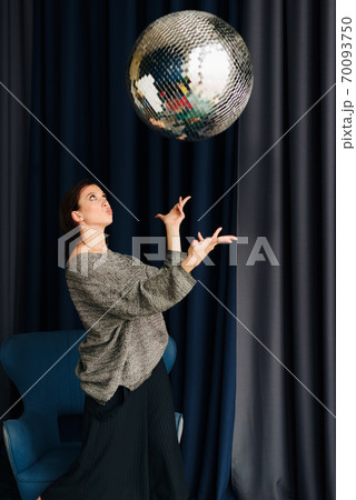 Beautiful young woman in grey sweater and disco ball at home 70093750