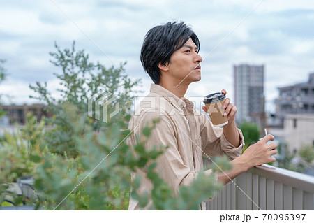 ビルの屋上で飲み物を飲みながら電子タバコをすう若い男性 ビルの屋上で飲み物を飲みながら電子タバコをすう若い男性 70096397